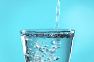 Crystal-clear alkaline ionized water pouring into a glass, with bubbles forming as the water fills the glass, highlighting its purity and freshness